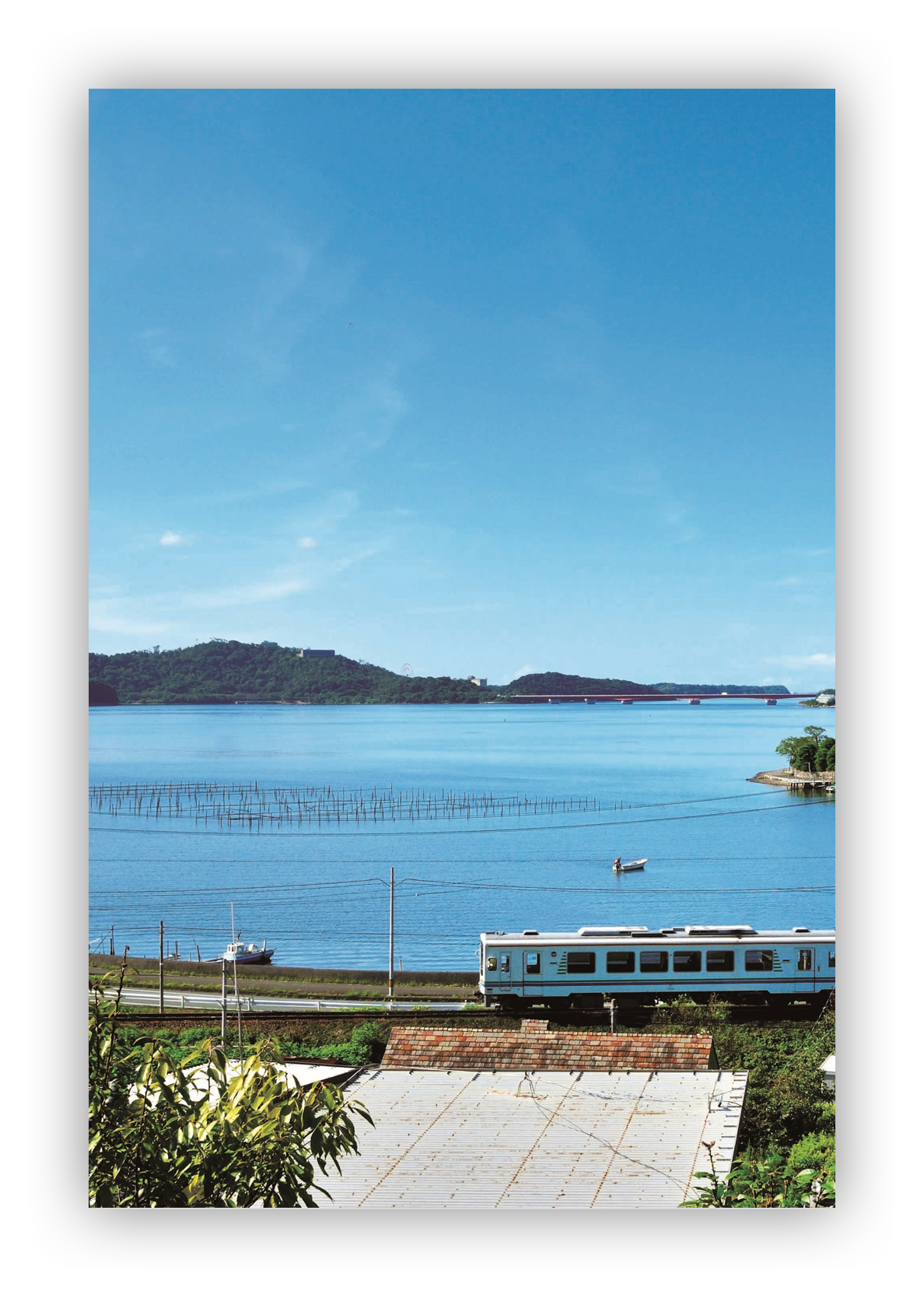 A train passes along the edge of Lake Hamana. A bridge can be seen crossing it in the distance.